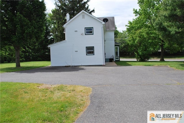 back of house featuring a chimney, a yard, and driveway