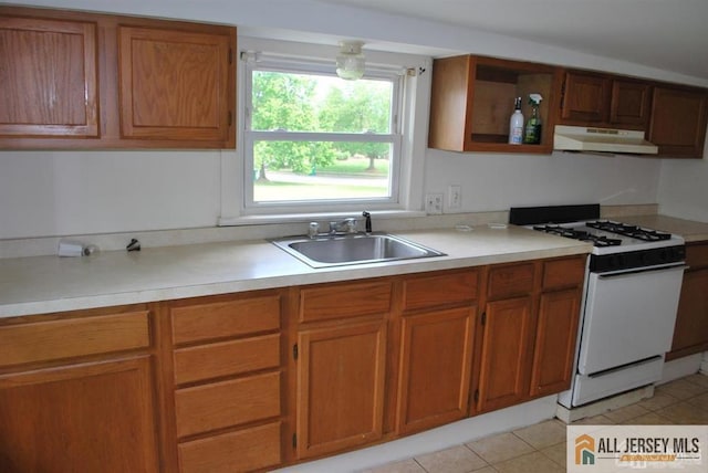 kitchen featuring white gas range, brown cabinets, light countertops, a sink, and under cabinet range hood