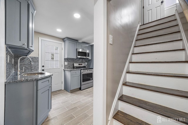 kitchen featuring decorative backsplash, stainless steel appliances, sink, dark stone countertops, and light hardwood / wood-style floors