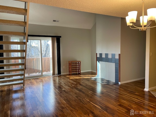 unfurnished room with a textured ceiling, dark wood-type flooring, a chandelier, and a fireplace