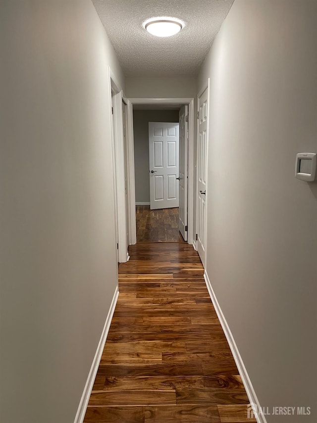 corridor with a textured ceiling and dark hardwood / wood-style floors