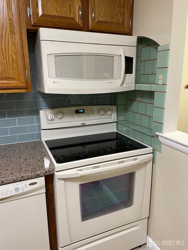 kitchen with decorative backsplash, dark stone counters, and white appliances