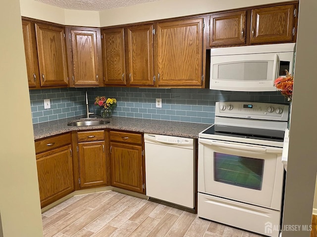 kitchen with light hardwood / wood-style floors, tasteful backsplash, white appliances, dark stone countertops, and sink