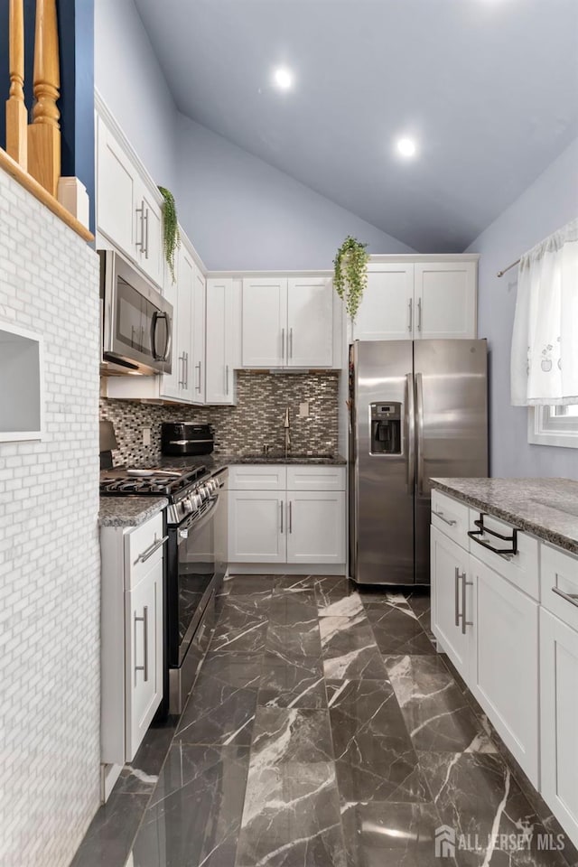kitchen featuring appliances with stainless steel finishes, lofted ceiling, tasteful backsplash, a sink, and white cabinetry