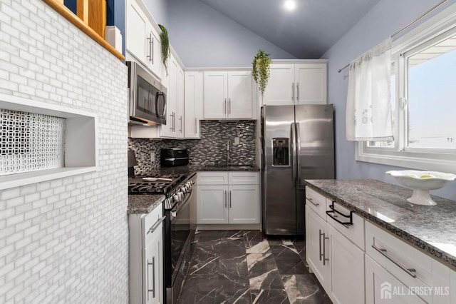 kitchen featuring appliances with stainless steel finishes, a sink, dark marble finish floors, lofted ceiling, and white cabinetry