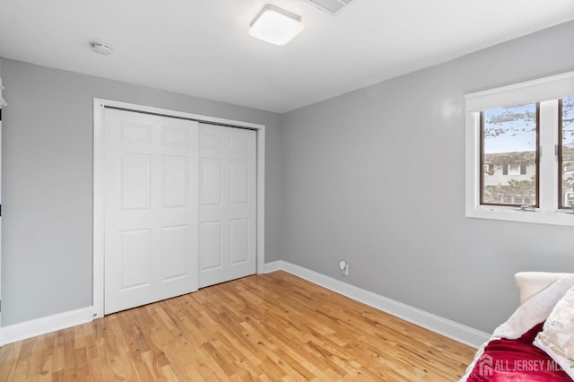 unfurnished bedroom featuring light wood-type flooring, baseboards, and a closet