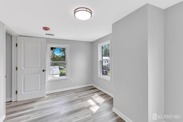 empty room with healthy amount of natural light, light wood finished floors, and baseboards