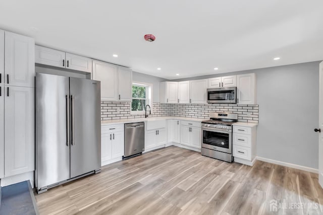 kitchen with appliances with stainless steel finishes, light countertops, decorative backsplash, light wood-style floors, and recessed lighting
