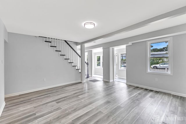 unfurnished living room featuring stairway, healthy amount of natural light, wood finished floors, and baseboards