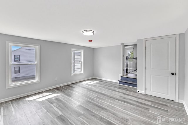 spare room featuring light wood-style floors, baseboards, and stairway