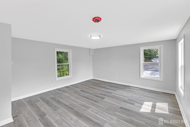 empty room with plenty of natural light, wood finished floors, and baseboards