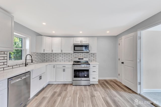 kitchen with stainless steel appliances, white cabinetry, light wood-type flooring, backsplash, and recessed lighting