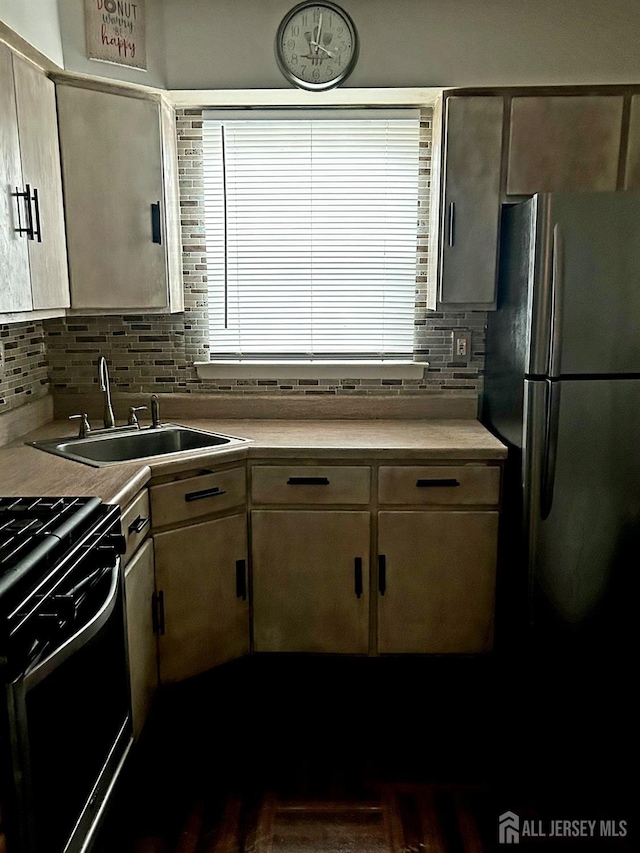 kitchen featuring black gas range, decorative backsplash, freestanding refrigerator, light countertops, and a sink