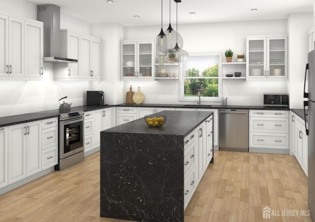 kitchen featuring appliances with stainless steel finishes, light wood-type flooring, hanging light fixtures, wall chimney range hood, and a center island