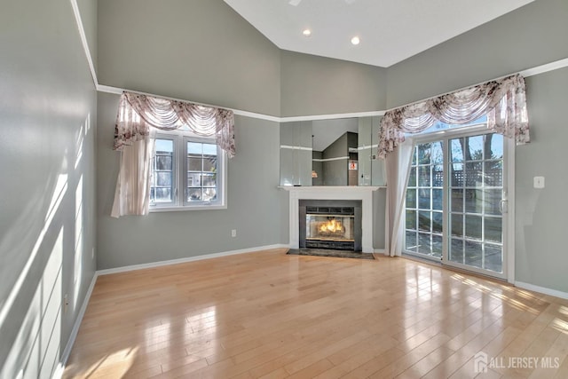 unfurnished living room featuring light wood-style floors, a fireplace with flush hearth, baseboards, and high vaulted ceiling