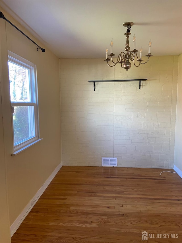 unfurnished dining area with a notable chandelier and wood-type flooring