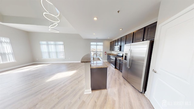 kitchen with light wood finished floors, dark brown cabinets, baseboards, light stone counters, and appliances with stainless steel finishes