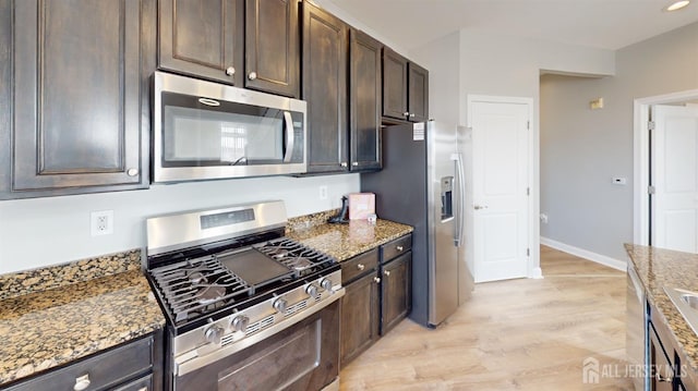 kitchen with light stone counters, baseboards, stainless steel appliances, dark brown cabinetry, and light wood-type flooring