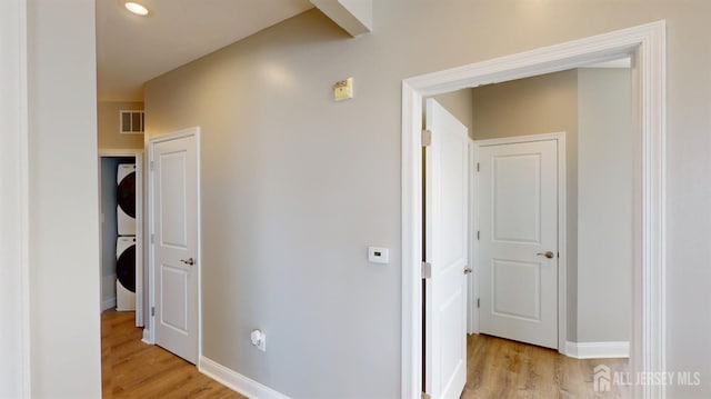 hallway featuring baseboards, light wood-style flooring, and stacked washing maching and dryer