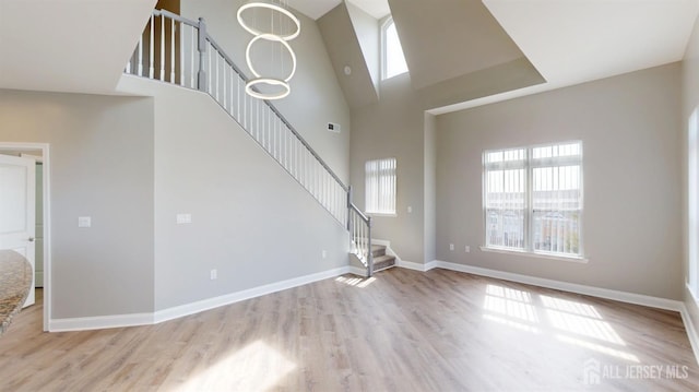 unfurnished living room with stairway, wood finished floors, baseboards, and a towering ceiling