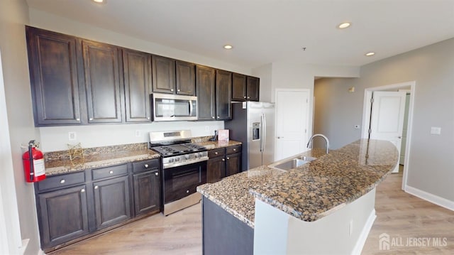 kitchen with stone counters, recessed lighting, appliances with stainless steel finishes, light wood-style flooring, and a sink