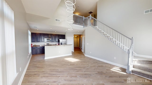 unfurnished living room featuring visible vents, baseboards, stairs, and light wood finished floors