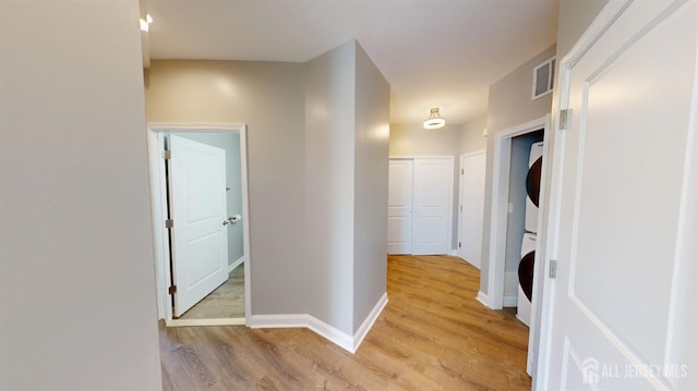 hall with visible vents, stacked washer and clothes dryer, baseboards, and light wood-style floors