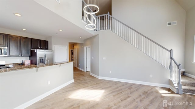 kitchen with visible vents, light wood-type flooring, a kitchen breakfast bar, stainless steel appliances, and baseboards