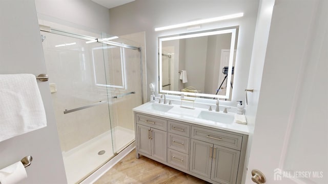 full bath featuring double vanity, wood finished floors, a stall shower, and a sink