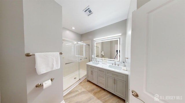 full bath with visible vents, double vanity, a stall shower, wood finished floors, and a sink