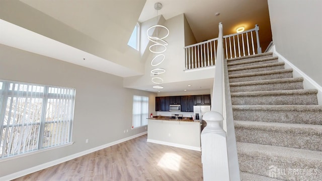 staircase with wood finished floors, baseboards, and a towering ceiling