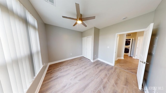 unfurnished bedroom with visible vents, light wood-style flooring, stacked washer and clothes dryer, and baseboards