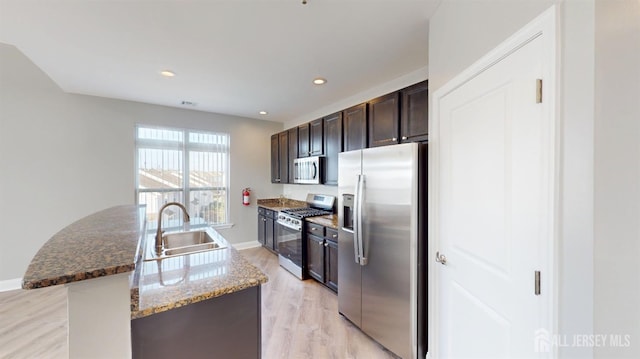 kitchen featuring light wood finished floors, a kitchen island with sink, a sink, stainless steel appliances, and dark brown cabinets