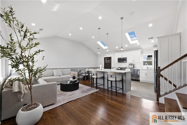 living room with vaulted ceiling with skylight, dark hardwood / wood-style floors, and sink