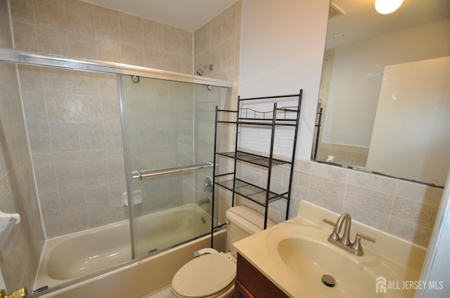 full bathroom with tile walls, vanity, toilet, shower / bath combination with glass door, and tasteful backsplash