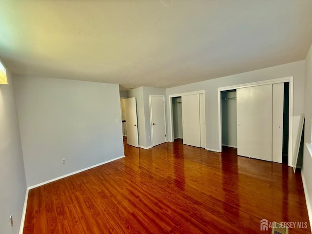 unfurnished bedroom with dark hardwood / wood-style flooring and multiple closets