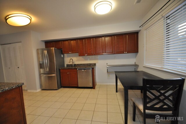 kitchen featuring stainless steel appliances, dark stone countertops, sink, and light tile patterned floors