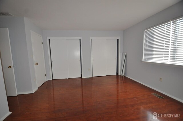 unfurnished bedroom featuring multiple closets and dark hardwood / wood-style flooring