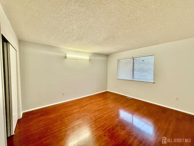 unfurnished bedroom featuring a closet, visible vents, baseboards, and wood finished floors