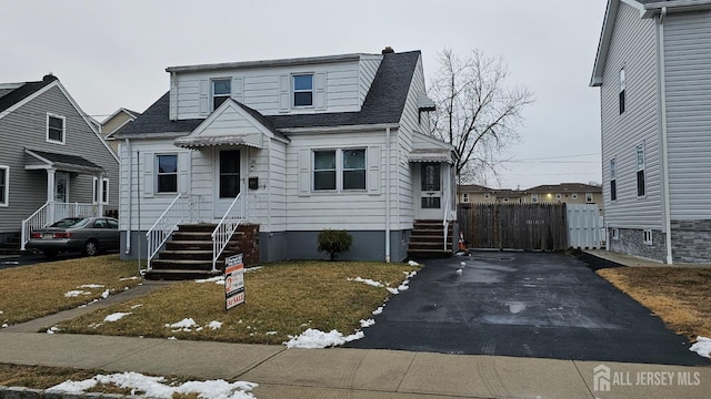 view of front of house with entry steps, driveway, a shingled roof, and fence