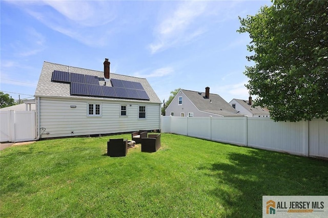 back of house with solar panels, a chimney, and roof with shingles