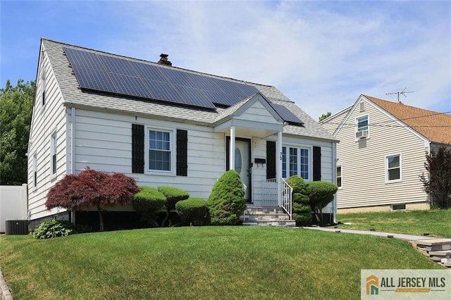 view of front facade with a front yard, solar panels, roof with shingles, and a chimney
