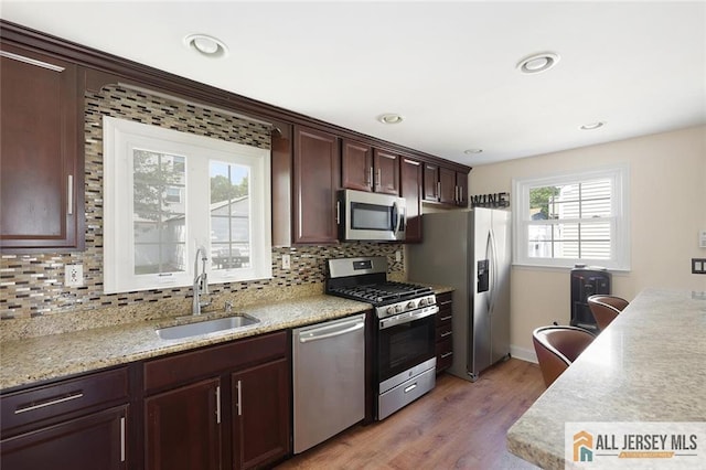 kitchen with stainless steel appliances, a sink, backsplash, light wood finished floors, and recessed lighting