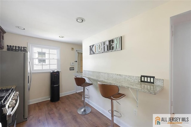 kitchen featuring stainless steel gas range, dark wood finished floors, a breakfast bar area, baseboards, and light stone countertops