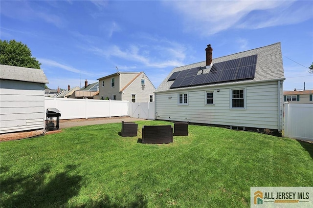rear view of property with roof mounted solar panels, roof with shingles, and a chimney