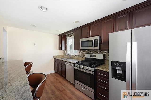 kitchen with stainless steel appliances, a sink, tasteful backsplash, dark wood finished floors, and dark brown cabinetry