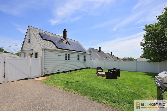back of house featuring a gate, roof mounted solar panels, a shingled roof, a fire pit, and a chimney