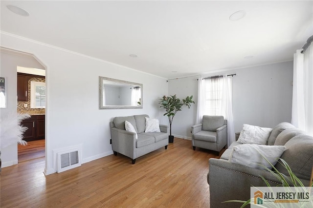 living room with light wood-style flooring, healthy amount of natural light, crown molding, and baseboards