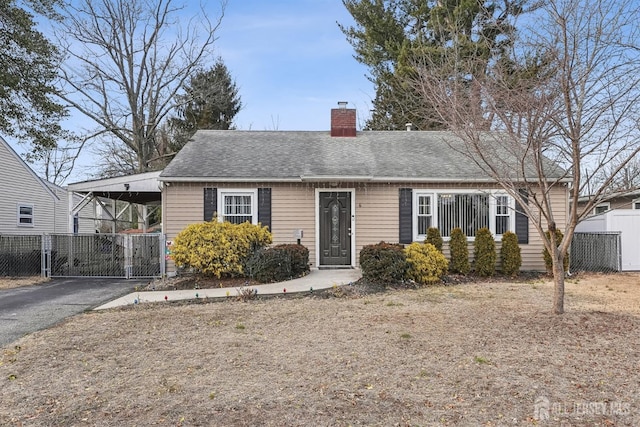 view of front of property featuring driveway, fence, roof with shingles, an attached carport, and a chimney