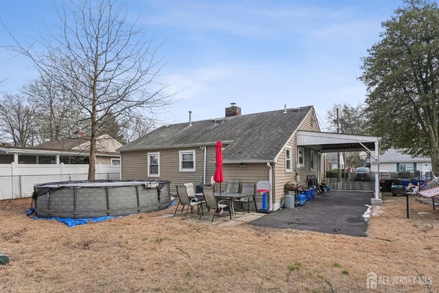 rear view of property with a fenced in pool, an attached carport, fence, roof with shingles, and a chimney